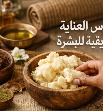 زبدة الشيا الخام والدلكة السودانية والأعشاب الطبيعية في أوعية خشبية، مع يد تمسك الزبدة، تمثل طقوس العناية الإفريقية للبشرة